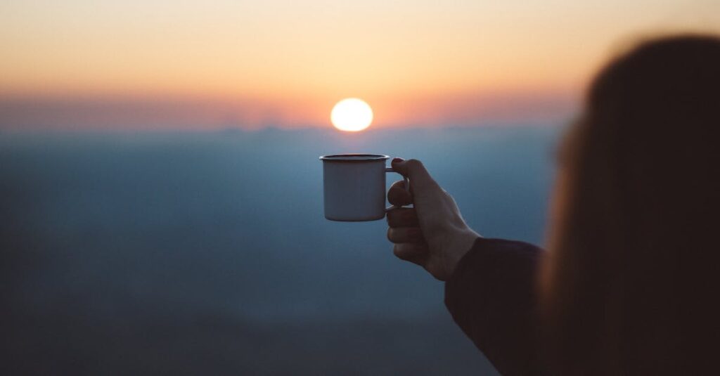 pexels-photo-1752806-1752806 A person holds a coffee cup against a beautiful sunrise, capturing a serene outdoor moment.